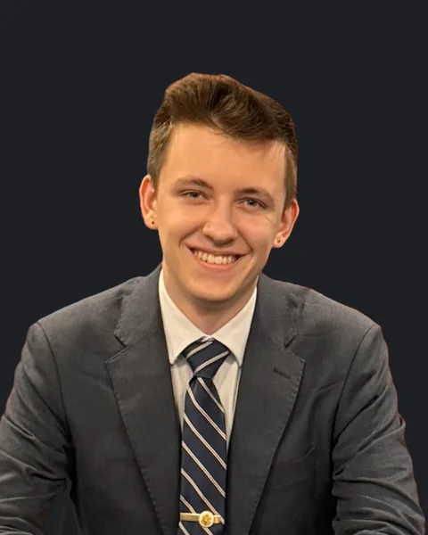 Lochlan McElroy, smiling, in a dark suit and striped tie